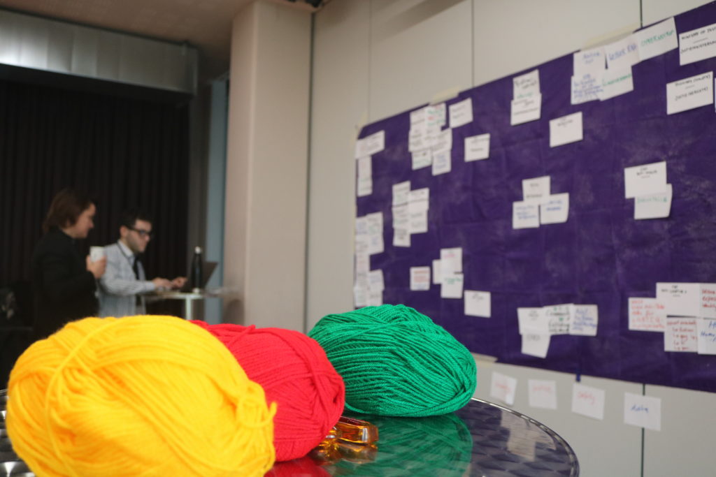Photo of wool in three colours in foreground, and sticky wall with notes in the background. 